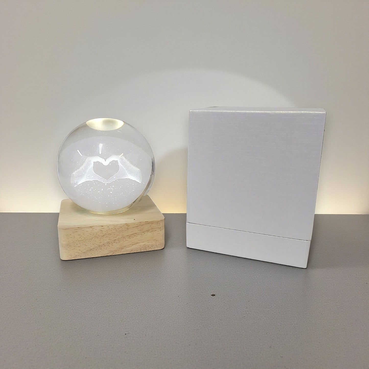 Sfera di cristallo luminosa con base in legno in tema mani a forma di cuore