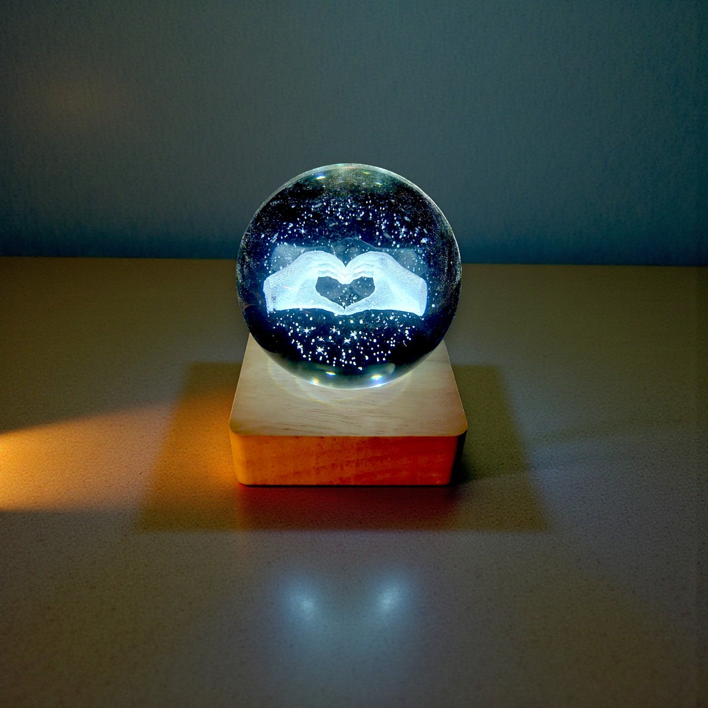 Sfera di cristallo luminosa con base in legno in tema mani a forma di cuore
