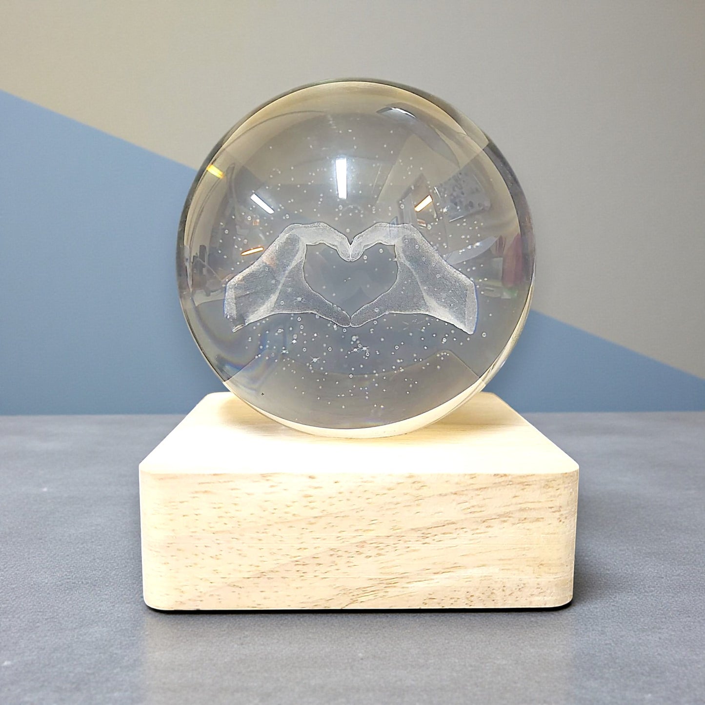 Sfera di cristallo luminosa con base in legno in tema mani a forma di cuore